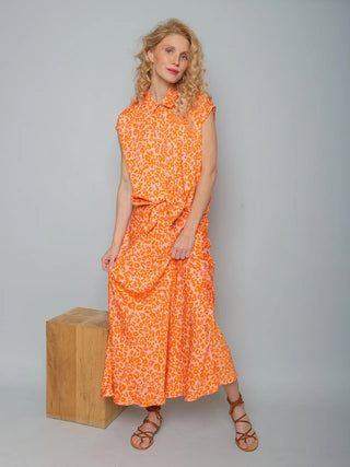 Emily Bluse 155690 orange/leo getragen von einer Frau, zeigt ein kurzärmeliges, geknotetes Blusentop mit sommerlichem Leoparden-Print in Orange-Pink, kombiniert mit einem fließenden Midi-Rock.
