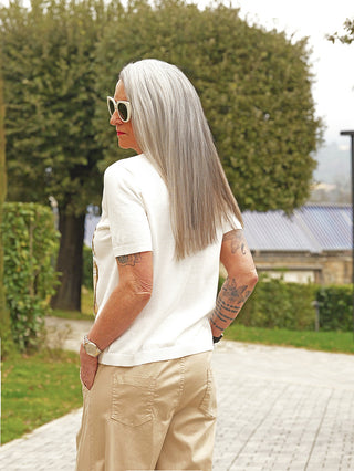 Person von hinten im OFF#DLY Feinstrick Finja white, mit kurzen Ärmeln und rundem Ausschnitt, Hände in Taschen, sichtbare Arm-Tattoos. Eleganter Feinstrick-Look, ideal für stilbewusste Frauen.