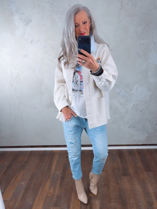 Person in Spiegelselfie trägt OFF#DLY Denim Milano lightblue, leicht zerstörte, hellgewaschene Slim-Jeans, die bis zum Knöchel reichen, kombiniert mit eleganten, beigefarbenen Stiefeletten und einem lässigen Overshirt.