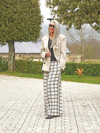 Frau im Freien trägt den OFF#DLY Blazer Modena beige, einen eleganten, leicht strukturierten, doppelreihigen Blazer mit klassischem Reverskragen, kombiniert mit einer schwarzen Hose für einen stilvollen Look.