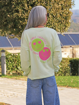 Eine Person trägt den OFF#DLY Sweat Happy mint, einen locker geschnittenen, leichten Sweatshirt mit zwei herzäugigen Smileys und dem Slogan auf der Rückseite, perfekt für entspannte Looks.