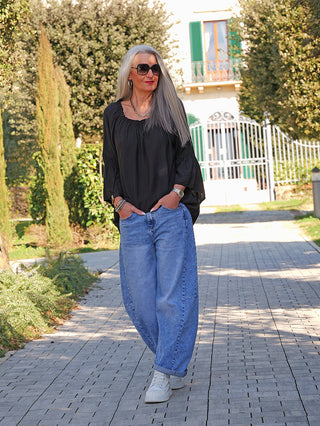 Frau trägt das OFF#DLY Shirt Garda black mit lockerem Schnitt und weitem, elastischem Ausschnitt, das auch off-shoulder getragen werden kann. Ergänzt durch voluminöse, volantbesetzte Ärmel.