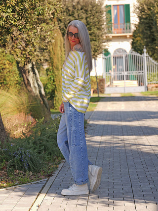 Frau trägt das OFF#DLY Ringel Grosso white/matcha Langarmshirt mit lockerer Passform und breiten Streifen auf einem Gartenweg. Kombiniert mit Jeans und weißen Sneakers, wirkt sie lässig-stylisch.
