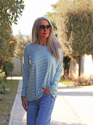 Eine Frau trägt das OFF#DLY Ringelshirt Frida mint/white, ein lässiges, locker fallendes Longsleeve mit feinen Streifen, während sie entspannt im Freien spaziert.