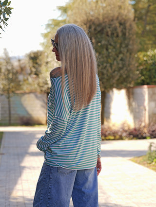 Person von hinten auf einem Weg, trägt das OFF#DLY Ringelshirt Frida mint/white mit mintgrünen und weißen Streifen, eine Schulter frei, kombiniert mit blauer Jeans und einem Armband.