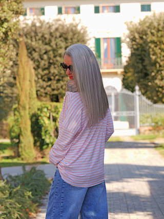 Eine Person trägt das OFF#DLY Ringelshirt Frida rosa/white, ein locker fallendes, gestreiftes Longsleeve mit einer lässigen Passform und offener Schulter, ideal für stilvolle Casual-Looks.