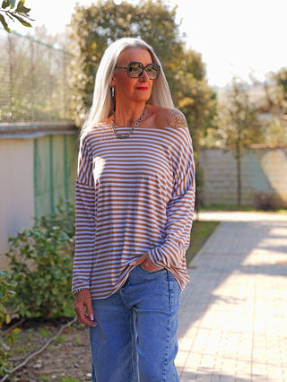 Person trägt das OFF#DLY Ringelshirt Frida white/camel mit horizontalen Streifen. Das lässige, langärmelige Oberteil betont ihren urbanen Stil, kombiniert mit Jeans und einer auffälligen Kette.