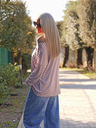 Frau trägt das OFF#DLY Ringelshirt Frida white/camel mit horizontalen Streifen und offener Schulterpartie, kombiniert mit blauer Jeans. Ideal für lässige, stilvolle Alltagslooks.