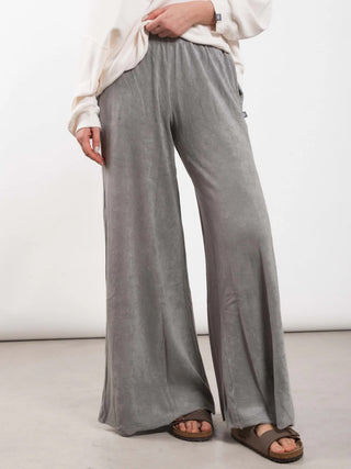 Person trägt Outryght Aou T grey moon Hose: locker geschnittene, weite Loungehose. Kombiniert mit einem cremefarbenen Oberteil und braunen Kork-Slides.