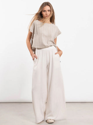 Junge Frau trägt eine Outryght Niki Gravel striped Bluse mit feinen vertikalen Streifen, kombiniert mit weit geschnittenen, hoch taillierten Hosen. Ihre Pose ist lässig mit Händen in den Hosentaschen.