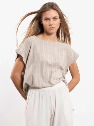 Eine junge Frau trägt das Outryght Niki Gravel striped Oberteil, ein locker sitzendes, kurzärmliges Shirt mit dezenten Streifen, kombiniert mit weiten Hosen, die Hände lässig in den Taschen.