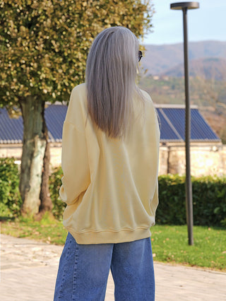 Eine Person trägt den OFF#DLY Sweater Star yellow/pink, einen locker sitzenden, lässigen Pullover, während sie auf einem gepflasterten Weg im Freien steht.