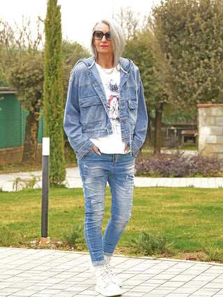 Frau in OFF#DLY Denimjacke Elin midblue, casual über weißem T-Shirt und Jeans, mit weißen Sneakern. Die Jacke hat einen lässigen, boxy Schnitt und große Taschen.