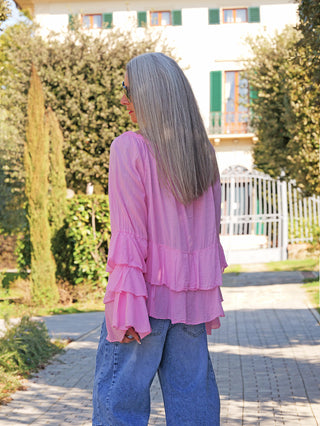 Person von hinten in OFF#DLY Blusenshirt Nena pink mit lockeren, gestuften Volantärmeln, kombiniert mit weit geschnittener blauer Jeans. Lässiger, femininer Look, ideal für sommerliche Hippie-Vibes.