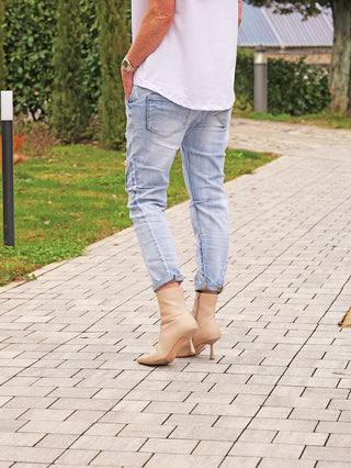 Person trägt die OFF#DLYDenim Destroy Camo lightblue. Die Jeans mit Destroyed-Look und Camo-Patches ist lässig gestylt mit hellen Waschungen, kombiniert mit nudefarbenen Stiefeletten auf einem gepflasterten Weg.