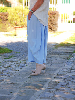 Person trägt OFF#DLY Pant Andrea blue, eine locker fallende Wide-Leg-Hose aus Lyocell, mit elastischem Bund und Gürtel. Die Hand in der Tasche, kombiniert mit eleganten Stiefeletten.