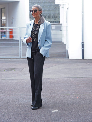 Ältere Frau trägt den OFF#DLY Blazer Venezia lightblue, ein eleganter, oversized Blazer mit klassischem Reverskragen, kombiniert mit einem schwarzen Top und fließenden, schwarzen Hosen auf einer städtischen Straße.