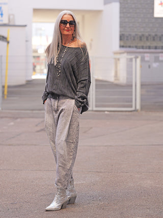 Ältere Frau trägt OFF#DLY Denim Venedig grey, locker geschnittene, hoch taillierte Baggy-Jeans mit verwaschenem Look, kombiniert mit grauem Strickpullover und silbernen Stiefeletten in urbaner Umgebung.