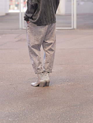 Person in OFF#DLY Denim Venedig grey, locker sitzende, leicht verwaschene Hose mit elastischem Bund, kombiniert mit silbernen Stiefeletten und dunklem Strickpullover, auf Asphalt stehend.