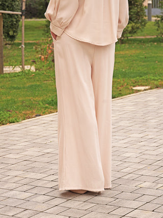 Person trägt die OFF#DLY Hose Bari vanille, eine weit geschnittene, fließende Hose mit Seitentaschen und Kordelzug, passend für einen entspannten und eleganten Look im Freien.