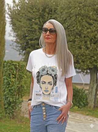Eine reife Frau trägt das OFF#DLY Tee Fashion mit einem Frontprint FASHION, MUSIC REVOLUTION 2024, GLAMOUR, kombiniert mit hellblauen Jeans und einer goldenen Kette.