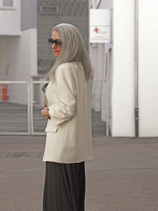 Die Frau trägt den OFF#DLY Blazer Dana beige, der durch seinen klassischen Reverskragen und die moderne Silhouette besticht, ideal für elegante und vielseitige Alltagskombinationen.