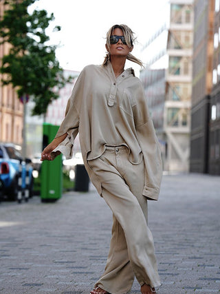Person trägt Gitta Banko Mali sand Bluse, oversized und lässig, auf urbaner Straße. Die Bluse hat klassischen Kragen, kurze Knopfleiste und Brusttasche, ideal für einen stilvollen Alltagslook.