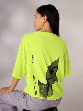 Person sitzt auf einem niedrigen Hocker, trägt LIV Bergen Tee Denmark neon yellow mit abstraktem schwarzen Grafik-Print und „liv bergen“ Logo am Rücken. Kombiniert mit hellgrauer Hose.