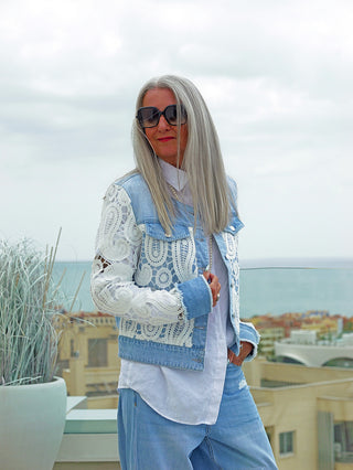 Eine Frau trägt die OFF#DLY Jacke Ibiza midbue/white, eine kurz geschnittene Denimjacke mit weißen Spitzeneinsätzen, ideal für einen stilvollen, femininen Look.