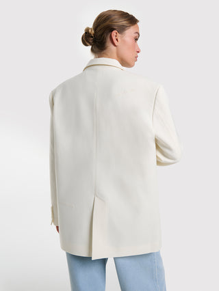 Rückansicht einer Frau im ALIX Flowy Oversized Blazer cream. Der Blazer hat eine mittige Rückennaht und einen leicht übergroßen Schnitt, perfekt kombiniert mit hellblauen Jeans.