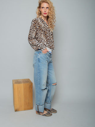 Model trägt die Emily Bluse 157500 leo: eine langärmelige, locker sitzende Shirtbluse mit Leopardenmuster und elastischem Strickbund. Kombiniert mit hochgeschnittenen Jeans und bunten, flachen Sandalen.