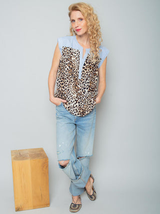 Emily Blusentop 158270 leo, ein modisches Blusentop mit Leopardenmuster und blauen Streifendetails, getragen von einer Frau mit lässig in die Taschen gesteckten Händen in distressed Jeans.