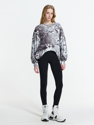 Junge Frau im #VDR Sweat 19046 black/white mit abstraktem Blumenmuster, lockerem Schnitt und voluminösen Ärmeln, kombiniert mit schwarzen Leggings und weißen, klobigen Stiefeln.