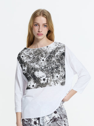 Junge Frau trägt #VDR Tee 19083 mit 3/4-Ärmeln und schwarz-weißem, abstraktem Blumenprint, kombiniert mit passenden Hosen, vor weißem Hintergrund, Hand in der Hüfte.