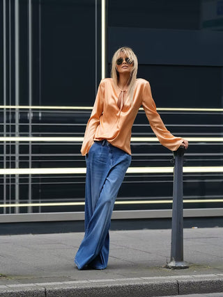 Gitta Banko Vivi Gold Rush: Eine Frau trägt weite Vivi Denim-Jeans in Gold Rush bei einem Street-Style-Shooting, kombiniert mit einer lockeren Bluse.