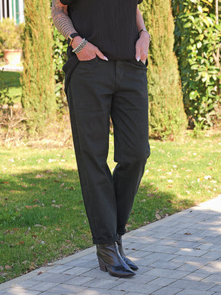 Person trägt OFF#DLY Denim black/black Lola, gerade geschnittene schwarze Jeans, umgeschlagene Säume, kombiniert mit schwarzen Lederstiefeln. Hände in Taschen, mit silbernen Armbändern und Uhr verziert.