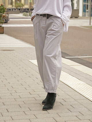 Person steht auf Gehweg in OFF#DLY Joggpant Zina grey; lockere, graue Hose mit leicht aufgerollten Bündchen, kombiniert mit schwarzem Gürtel und schwarzen Stiefeletten.