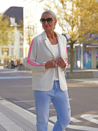 Frau in urbaner Umgebung trägt den OFF#DLYBlazer Oversized Stripes white mit sportiven Streifen an den Ärmeln und entspannter Passform über einem weißen Tanktop, kombiniert mit Jeans.