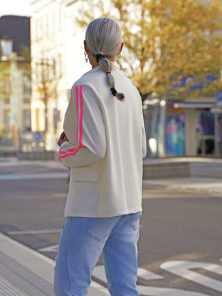 Person von hinten auf Gehweg mit einem OFF#DLYBlazer Oversized Stripes white, cremefarben mit pinken Streifen an den Ärmeln, kombiniert mit Jeans. Lässige, oversized Passform betont urbanen Streetstyle.
