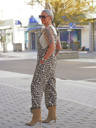Ältere Frau trägt OFF#DLY Musselin Latzhose leo mit Leopardenmuster, lockerem Schnitt und Knopfträgern, kombiniert mit einem hellen Tanktop und tanfarbenen Stiefeln auf städtischem Bürgersteig.