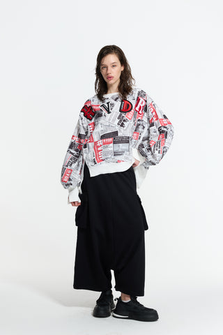 Model trägt #VDR Sweater 19033 white black mit Zeitungsausschnitten und roten Logo-Details, kombiniert mit weit geschnittenen, schwarzen Hosen und klobigen Sneakers, präsentiert in entspannter Pose.