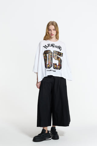 Junge Frau trägt das #VDR T-Shirt 19082 white mit Pleasing 05-Print, kombiniert mit weiten schwarzen Hosen und klobigen Sneakers, verkörpert lässigen Streetstyle und italienische Mode.