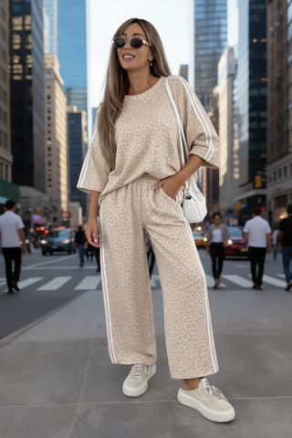 Junge Frau im OFF#DLY Anzug Rimini leo/beige: Oversize-Top mit 3/4-Ärmeln, weite Hose mit elastischem Bund und weißen Seitenstreifen, kombiniert mit Plattform-Sneakern und weißer Handtasche.
