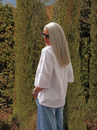 Eine Frau trägt das #VDR T-Shirt 19080 white mit „Inspire“-Print, Oversize-Schnitt und doppelten Ösen, kombiniert mit blauer Jeans und Sonnenbrille, vor grünen Sträuchern stehend.