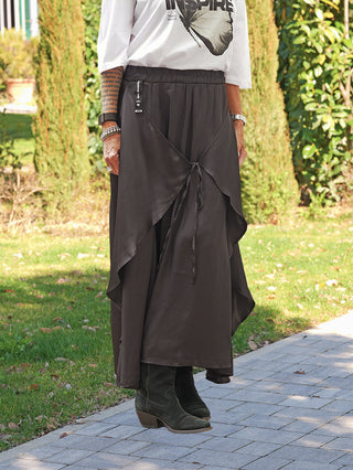 Person trägt #VDR Rock 19231 black, hoch tailliert mit Kordeldetail. Der Rock bietet eine fließende, asymmetrische Silhouette. Kombiniert mit schwarzen Stiefeletten für einen eleganten, modernen Look.