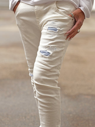 Nahaufnahme einer Person, die die OFF#DLY Denim Turin white trägt, mit dezenten Rissen am Oberschenkel. Die Hand mit silbernen Ringen steckt lässig in der vorderen Hosentasche.