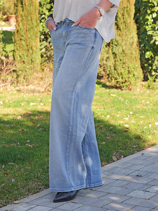 OFF#DLY Wide Leg Denim Giarra lightblue, getragen mit weitem Bein und umgeschlagenem Bund, kombiniert mit schwarzen Lederstiefeln auf einem Gartenweg.