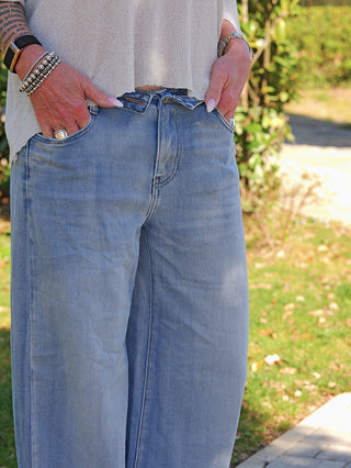 Person trägt OFF#DLY Wide Leg Denim Giarra lightblue mit weitem Bein und umgeschlagenem Bund, kombiniert mit einem leichten, kurz geschnittenen Oberteil. Accessoires umfassen Armbänder und eine Uhr.