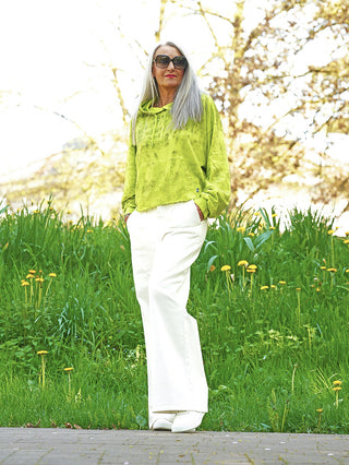 Frau in Outryght Celine neon green Hoodie mit lockerer Passform, kombiniert mit hochgeschnittenen weißen, weiten Hosen und weißen Slippern, Hände in den Taschen, steht auf einem gepflasterten Weg im Freien.