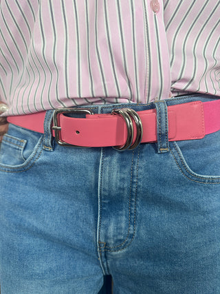 Nahaufnahme des OFF#DLY Stretch Gürtels fuchsia mit silberner Schnalle und Doppel-D-Ring-Detail, getragen mit einer pink-weiß gestreiften Bluse und hellblauer Jeans.